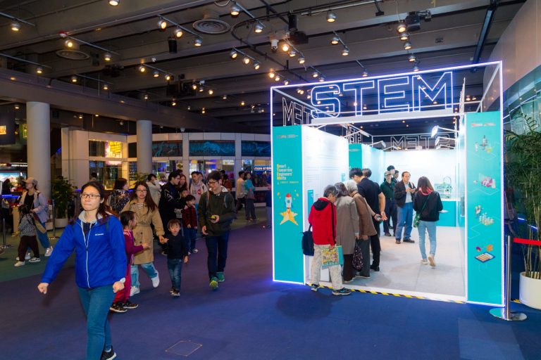 People visiting a STEM exhibition booth with illuminated signage and interactive displays.
